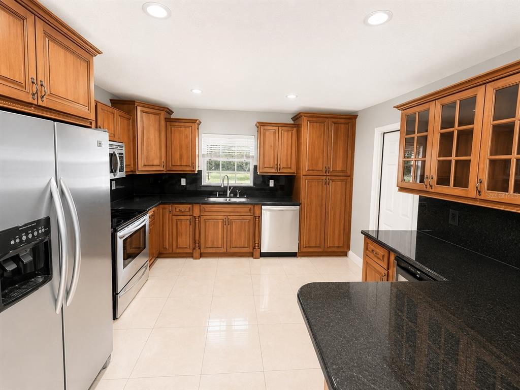 A kitchen features wood cabinets, black granite countertops, stainless steel appliances, and light tile flooring — 7126 SHEFFIELD DRIVE, LAKELAND, FL