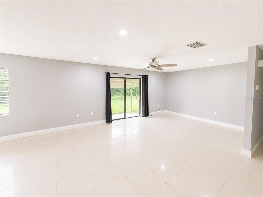 A spacious living room features light gray walls, white tile flooring, and sliding glass doors — 7126 SHEFFIELD DRIVE, LAKELAND, FL