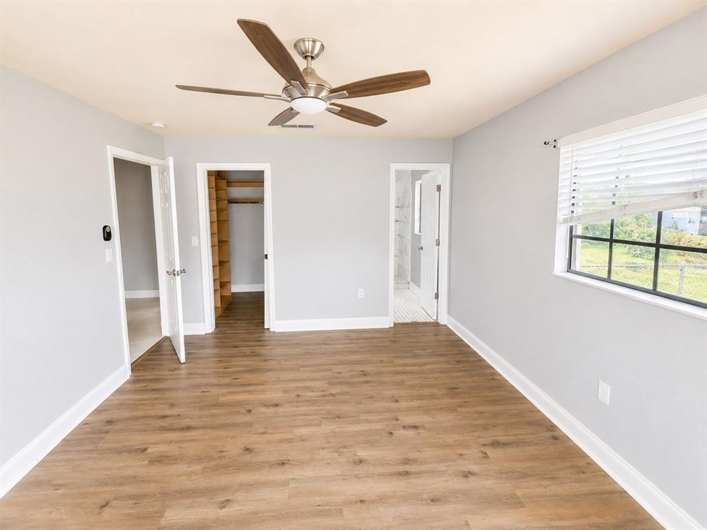 A bedroom with light gray walls, wood-look flooring, a ceiling fan, and two open doorways — 7126 SHEFFIELD DRIVE, LAKELAND, FL