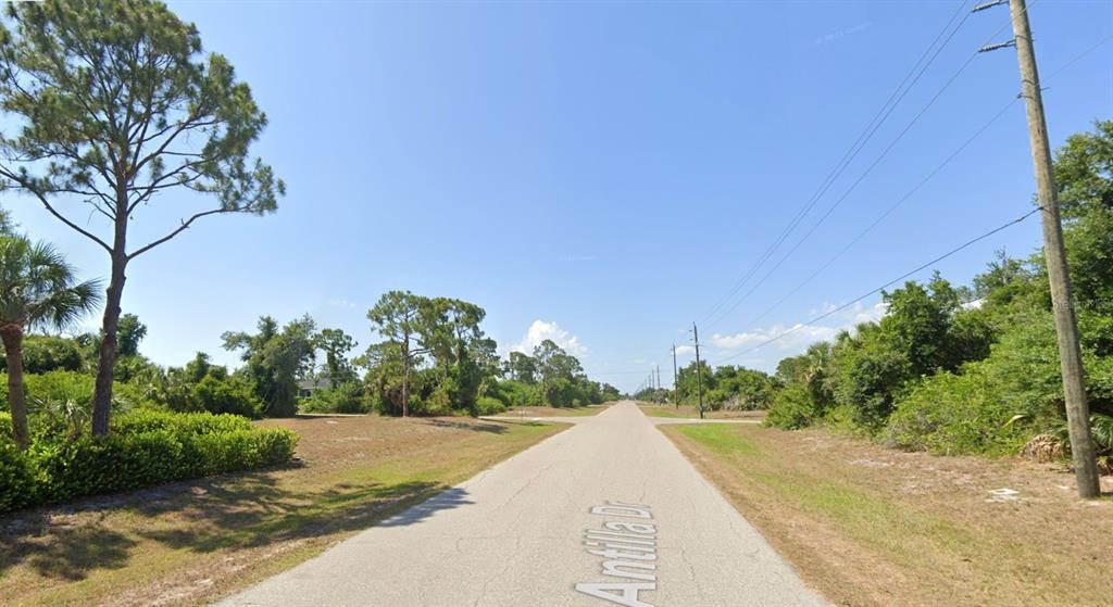 A paved road stretches through a wooded area with utility poles under a clear sky — 107 ANTILLA DRIVE, ROTONDA WEST, FL