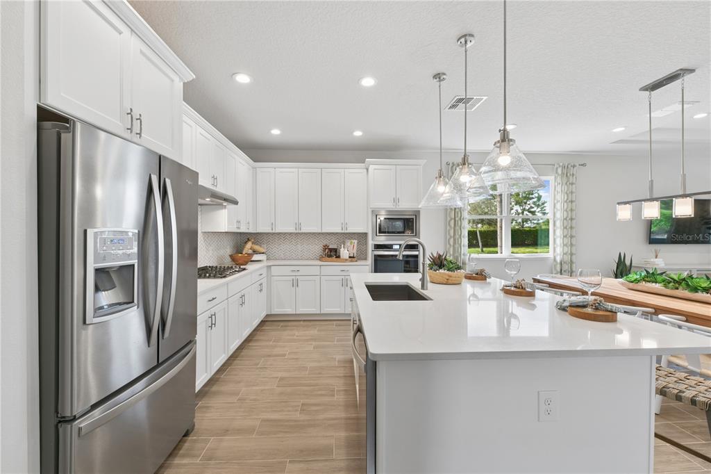 A modern kitchen features white cabinetry, stainless steel appliances, a large island, and tile flooring — 2418 PARK RIDGE STREET, APOPKA, FL