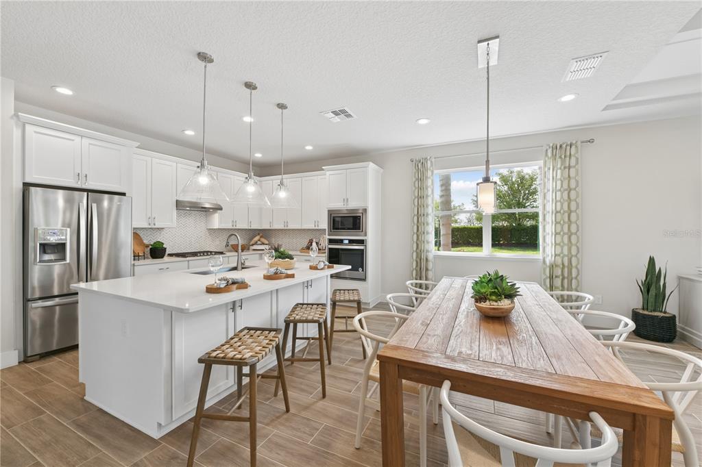 A kitchen features white cabinetry, a large island with bar stools, and a wooden dining table — 2418 PARK RIDGE STREET, APOPKA, FL