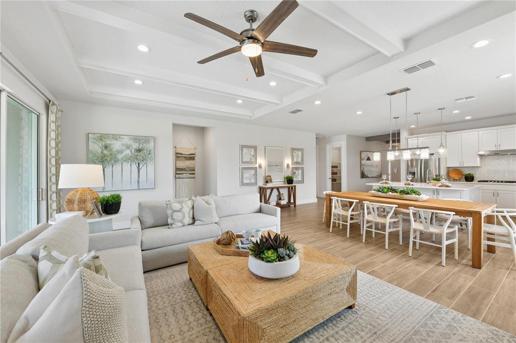 An open-concept living and dining area features a coffered ceiling, wood-look tile, and neutral furniture — 2418 PARK RIDGE STREET, APOPKA, FL
