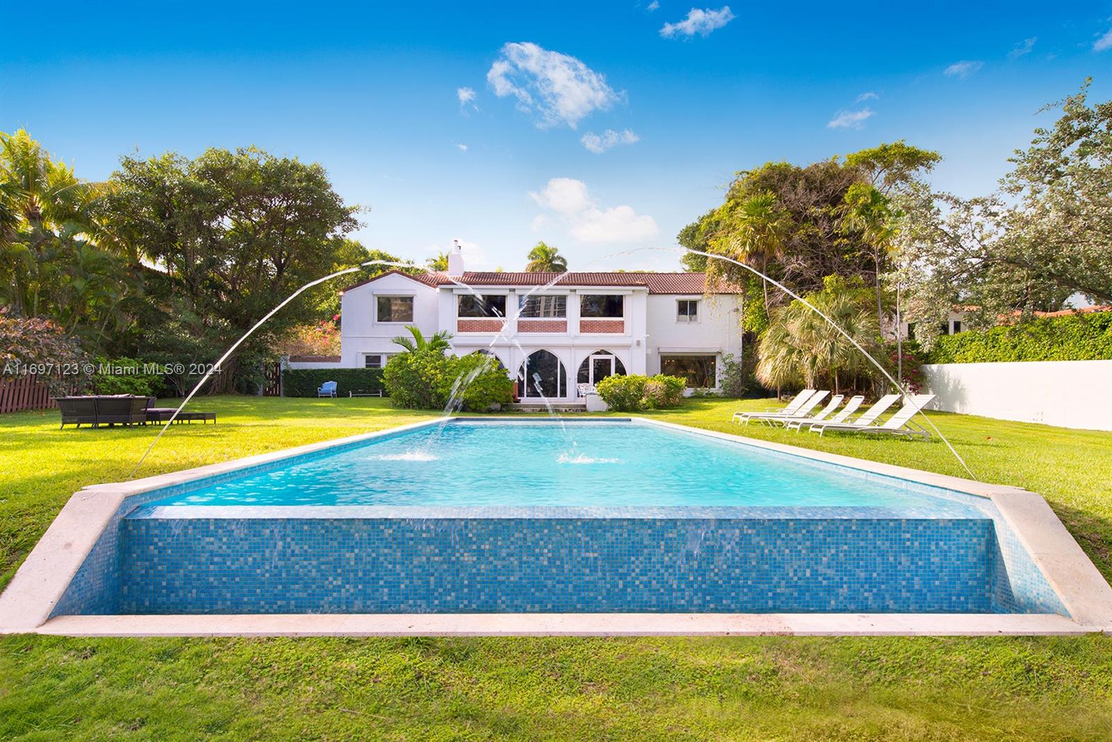 A backyard features a swimming pool with fountains and a two-story house with white walls — 4745 Pine Tree Dr, Miami Beach FL 33140, MIAMI BEACH, FL