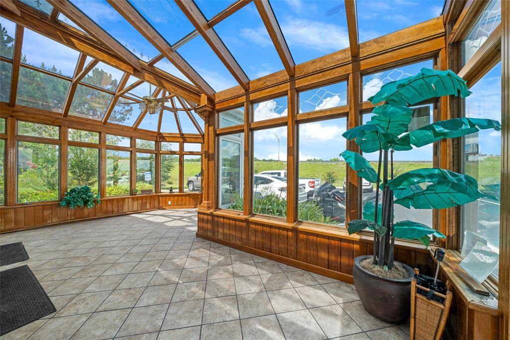 A sunroom with wood-framed glass walls, tile flooring, and a large potted artificial plant — 1720 NW 4TH AVENUE All Units, OCALA, FL