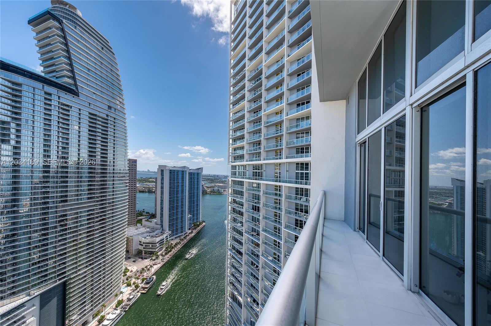 A high-rise balcony overlooks a narrow waterway between several modern glass skyscrapers — 475 Brickell Ave # 4115, Miami FL 33131, MIAMI, FL