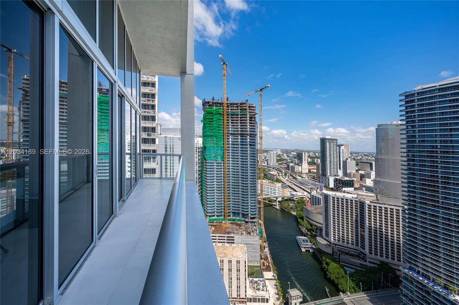 A high-rise balcony overlooks a city skyline, a river, and several construction sites with cranes — 475 Brickell Ave # 4115, Miami FL 33131, MIAMI, FL