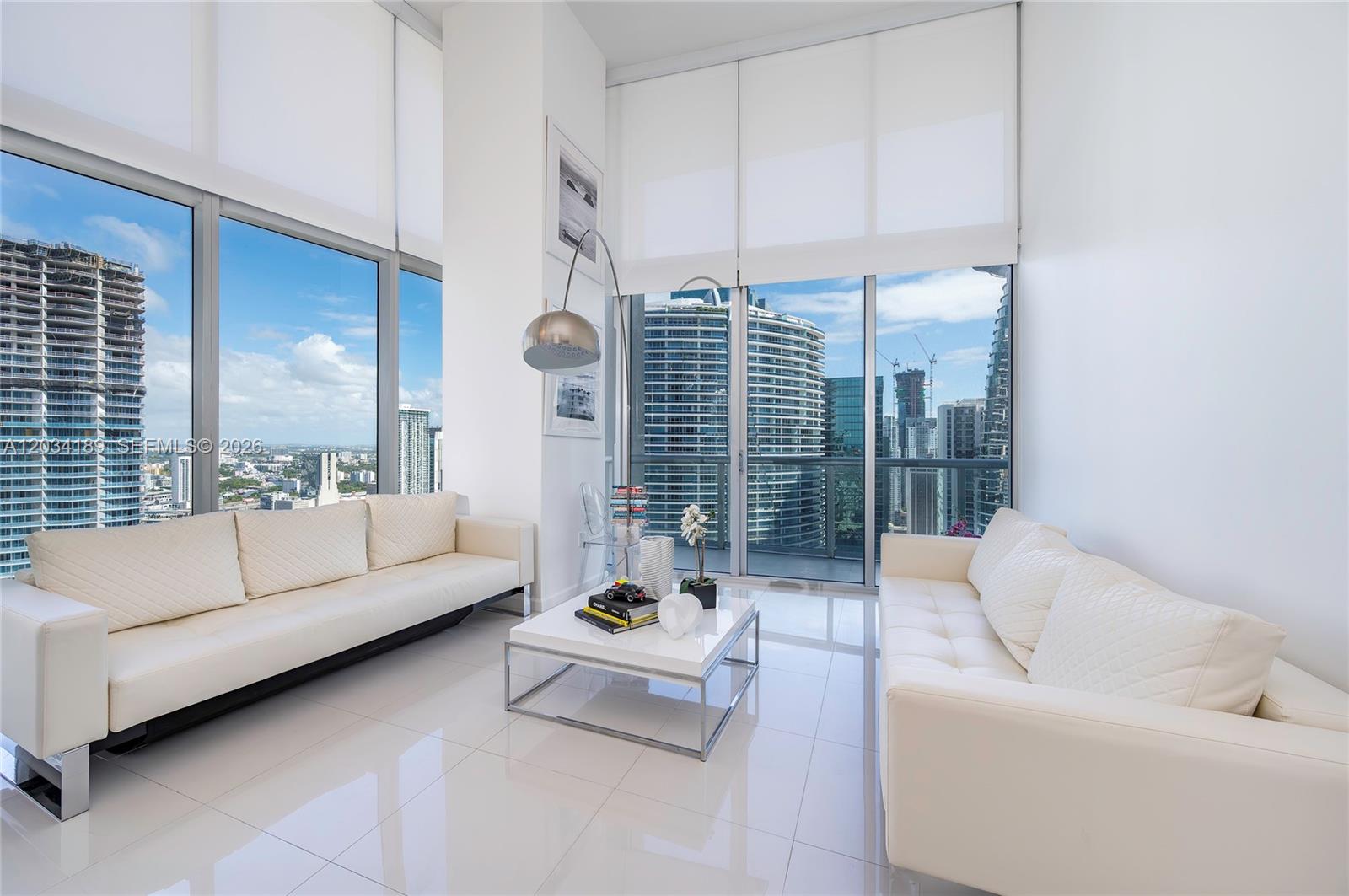 A modern living room features two white sofas, a glass coffee table, and floor-to-ceiling windows — 475 Brickell Ave # 4115, Miami FL 33131, MIAMI, FL