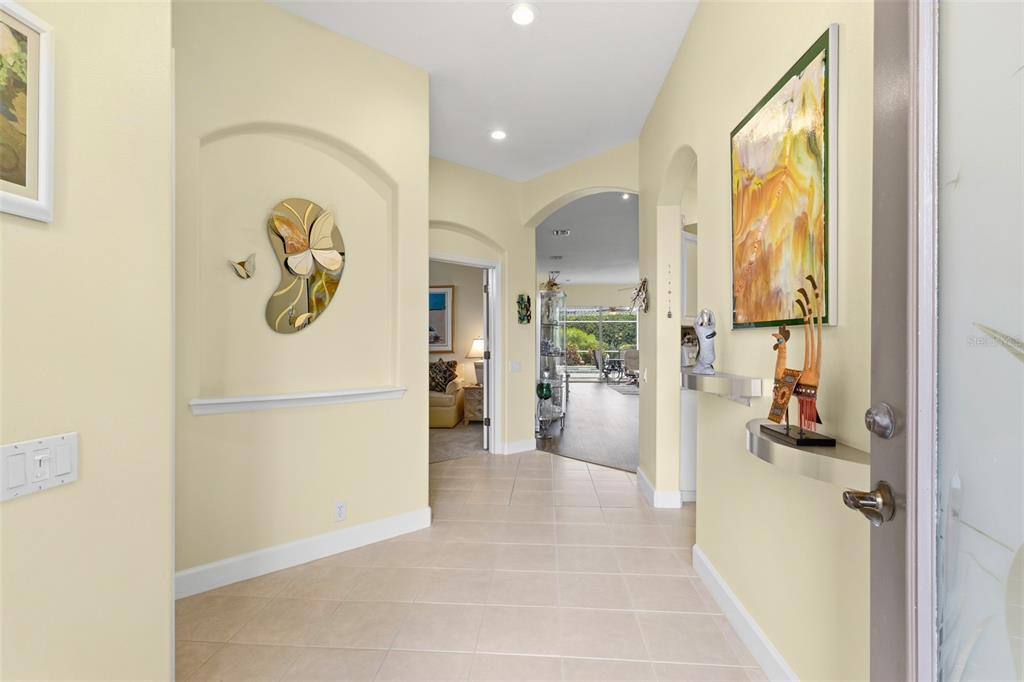 A bright foyer features tile flooring, arched wall niches, and a view into a living area — 5231 97TH STREET E, BRADENTON, FL