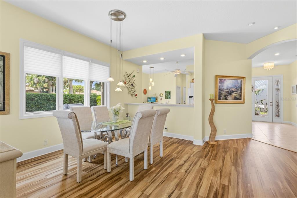 A dining area with a glass table, upholstered chairs, and wood flooring near a kitchen — 5231 97TH STREET E, BRADENTON, FL