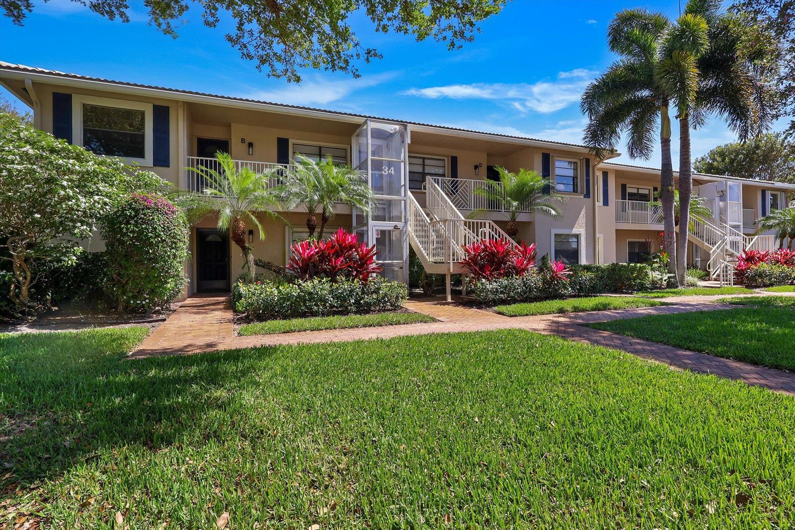 A two-story apartment building features a central glass elevator, exterior staircases, and landscaped gardens — 34 W Stratford Ln Lane W # D, Boynton Beach FL 33436, BOYNTON BEACH, FL