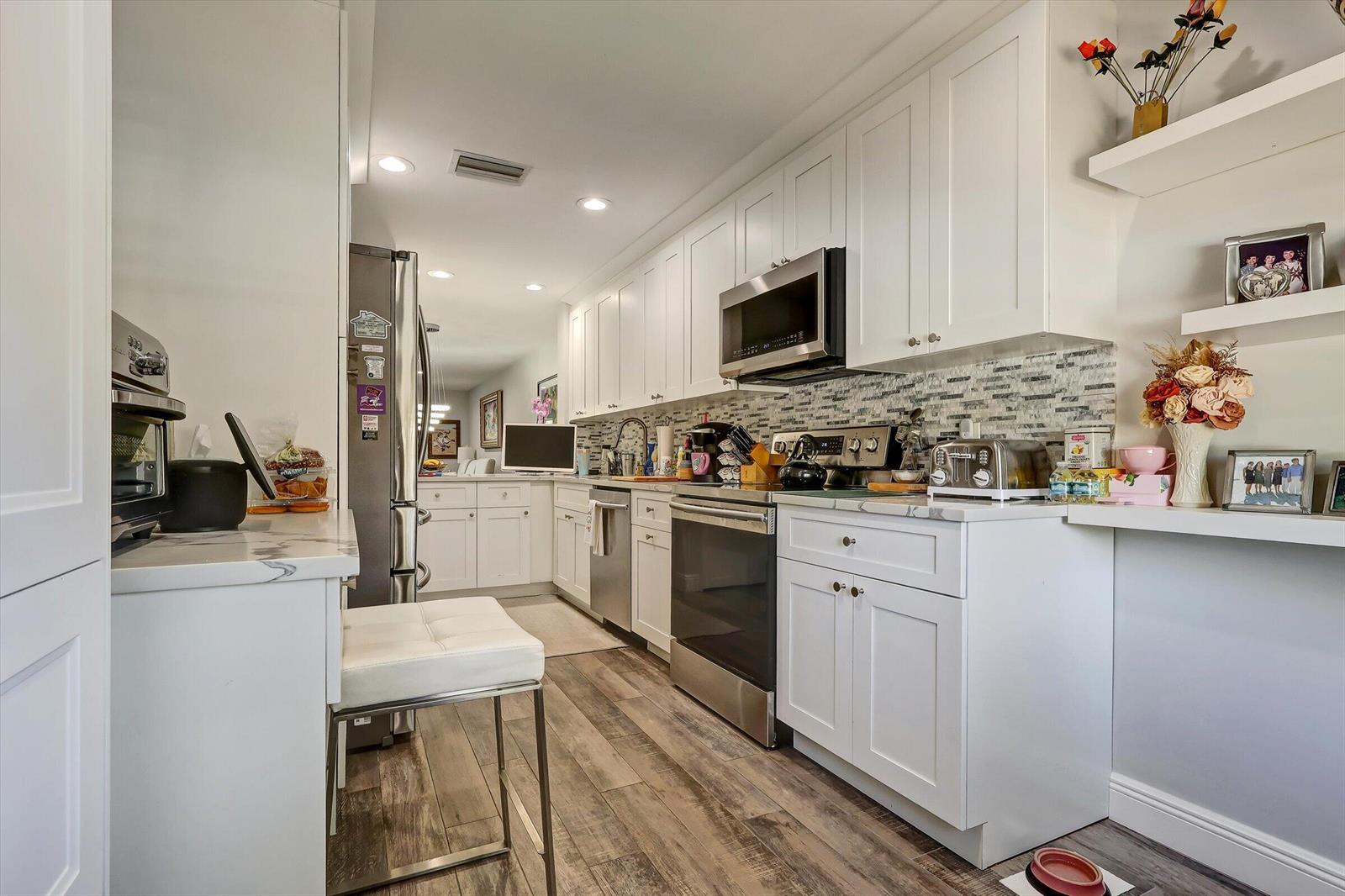 A galley kitchen features white cabinets, stainless steel appliances, and wood-look flooring — 34 W Stratford Ln Lane W # D, Boynton Beach FL 33436, BOYNTON BEACH, FL