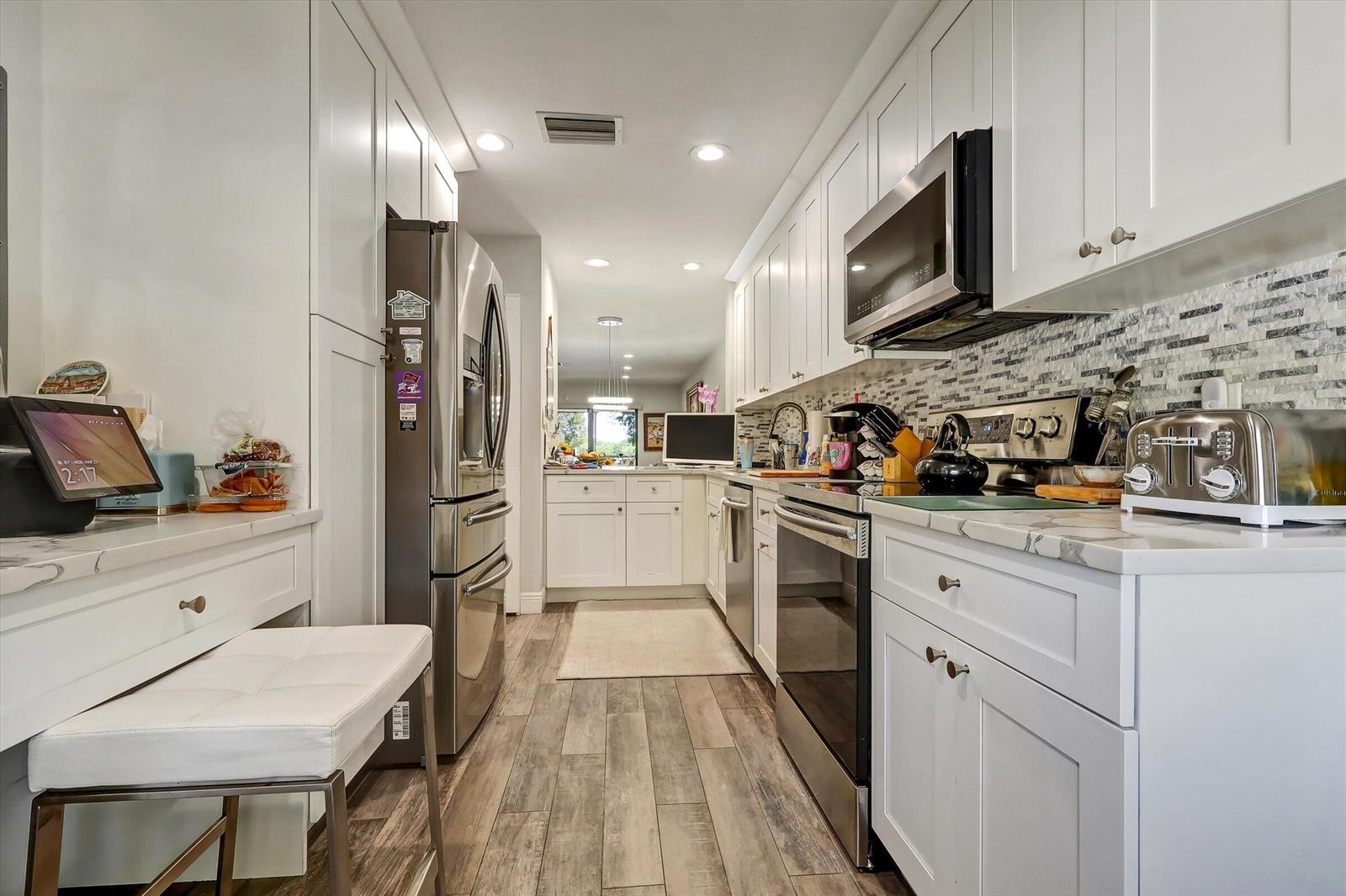 A galley kitchen features white cabinets, stainless steel appliances, marble-look countertops, and wood-plank flooring — 34 W Stratford Ln Lane W # D, Boynton Beach FL 33436, BOYNTON BEACH, FL