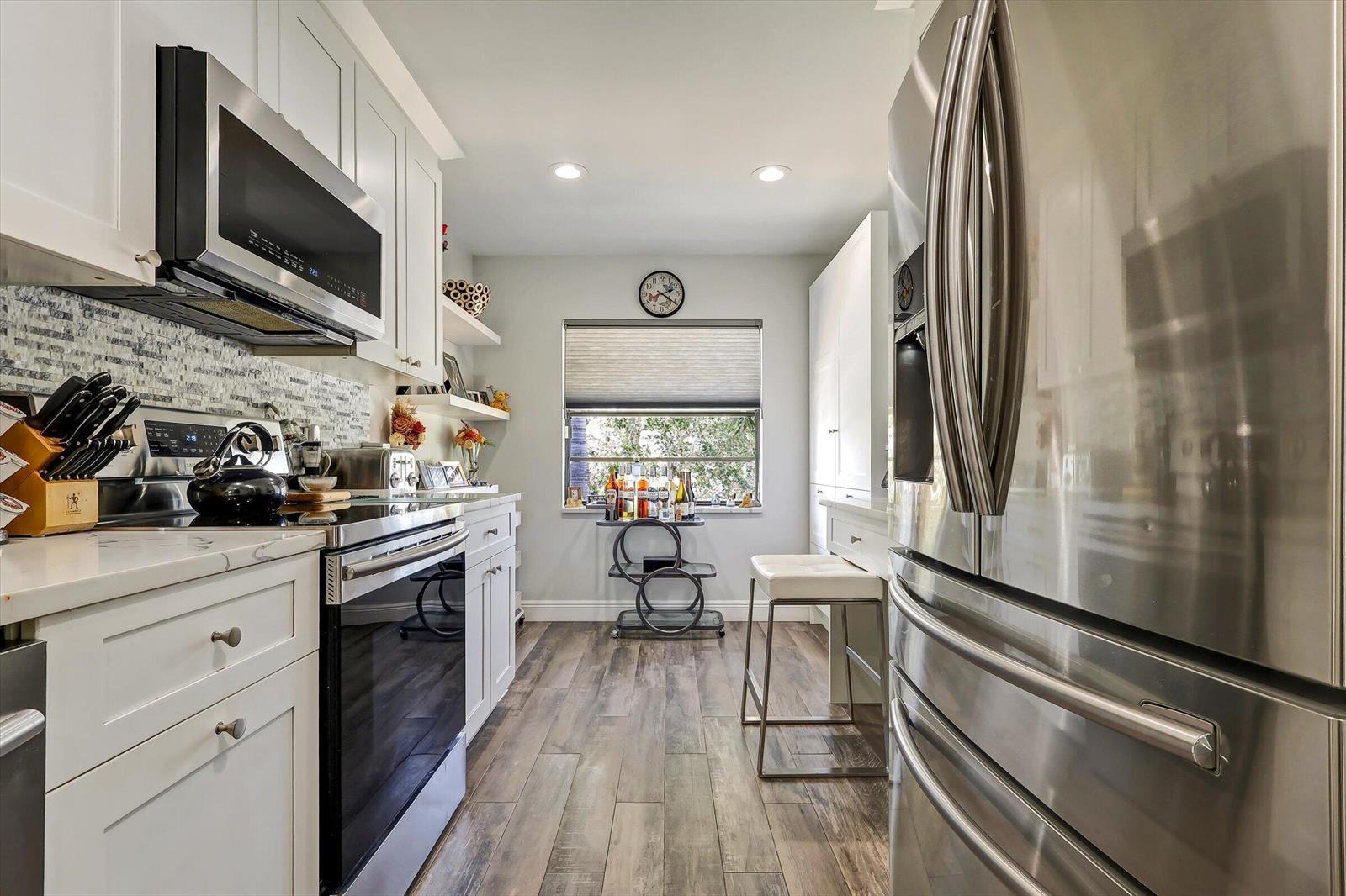 A galley kitchen features white cabinets, stainless steel appliances, a window, and wood-look flooring — 34 W Stratford Ln Lane W # D, Boynton Beach FL 33436, BOYNTON BEACH, FL
