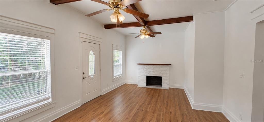 A living room features wood-look flooring, a white brick fireplace, and two ceiling fans — 8211 N 10TH STREET, TAMPA, FL