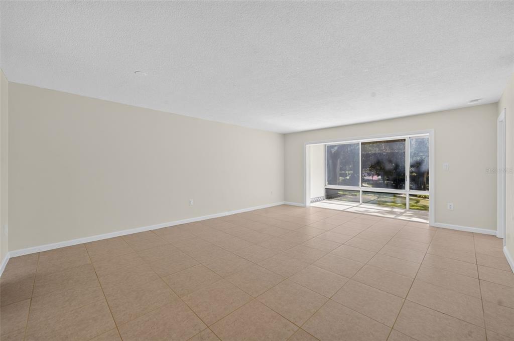 An empty living room features beige tile flooring, light-colored walls, and a large sliding glass door — 700 MELROSE AVENUE UNIT A5, WINTER PARK, FL
