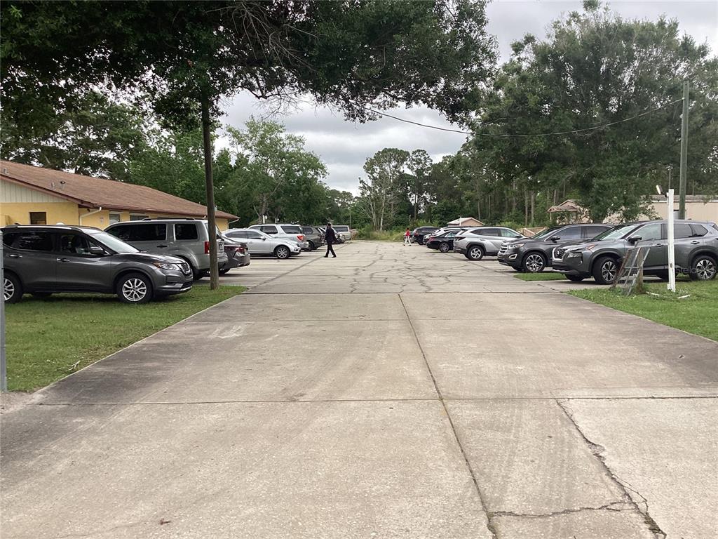 A concrete driveway lined with parked cars leads toward a wooded area under cloudy skies — 2270 JUPITER BLVD, PALM BAY, FL