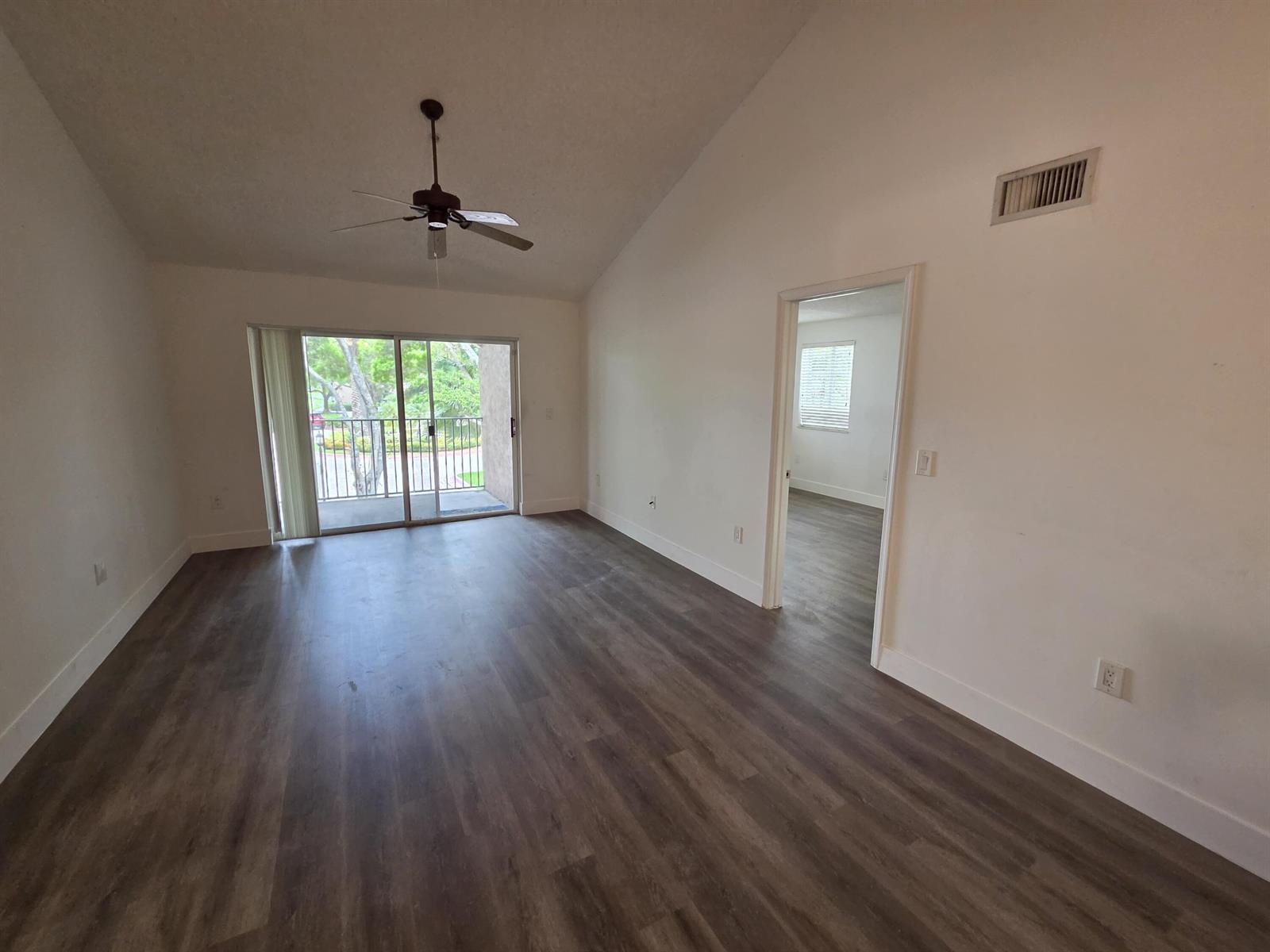 An empty living room with vaulted ceilings, a ceiling fan, sliding glass doors, and flooring — 12112 St.andrews Place # 212, Miramar FL 33025, MIRAMAR, FL