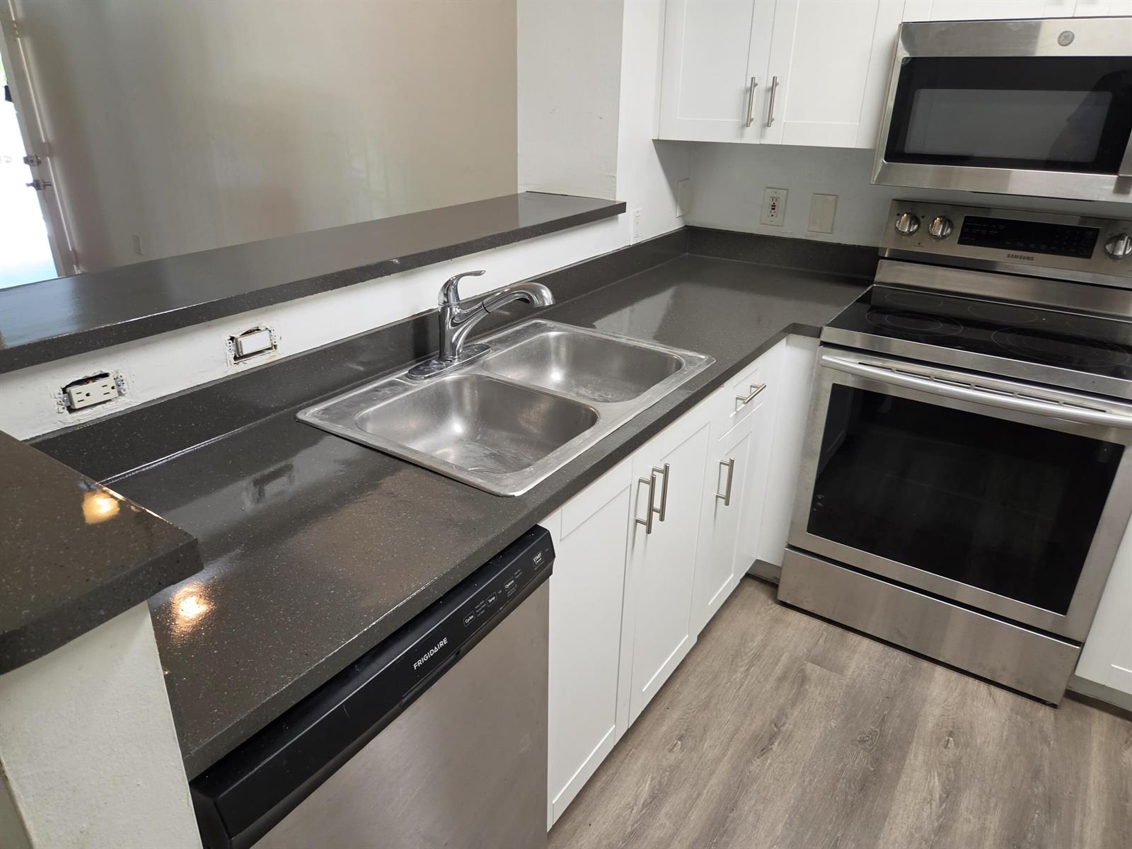 A kitchen features white cabinets, dark countertops, stainless steel appliances, and a double-basin sink — 12112 St.andrews Place # 212, Miramar FL 33025, MIRAMAR, FL