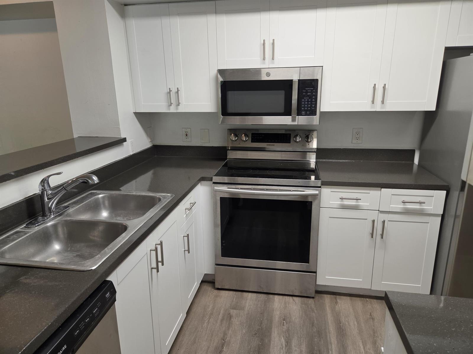A kitchen with white cabinets, dark countertops, stainless steel appliances, and wood-look flooring — 12112 St.andrews Place # 212, Miramar FL 33025, MIRAMAR, FL