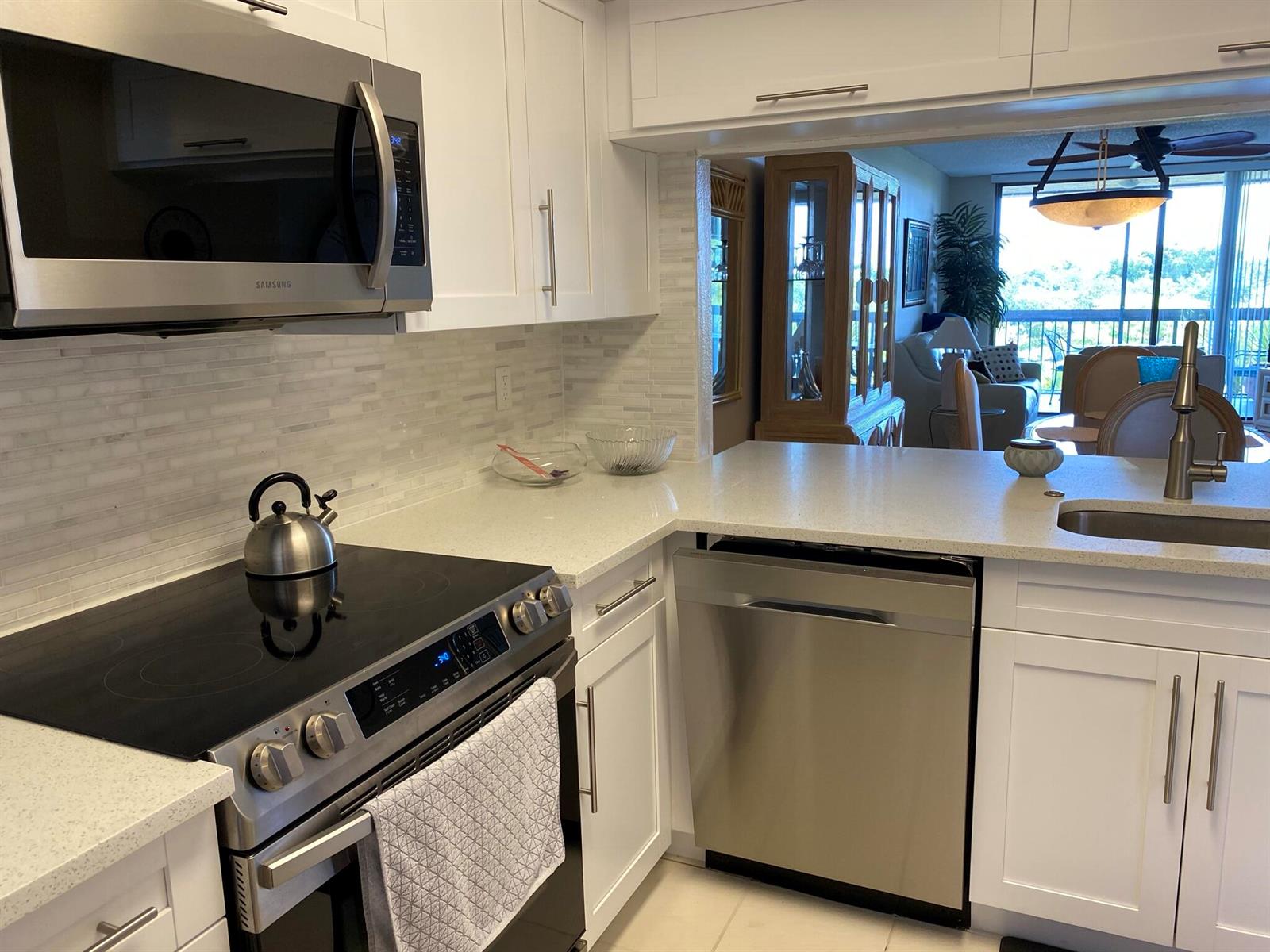 A kitchen with white cabinets, stainless steel appliances, quartz countertops, and a view into the living area — 600 Egret Circle # 7401, Delray Beach FL 33444, DELRAY BEACH, FL
