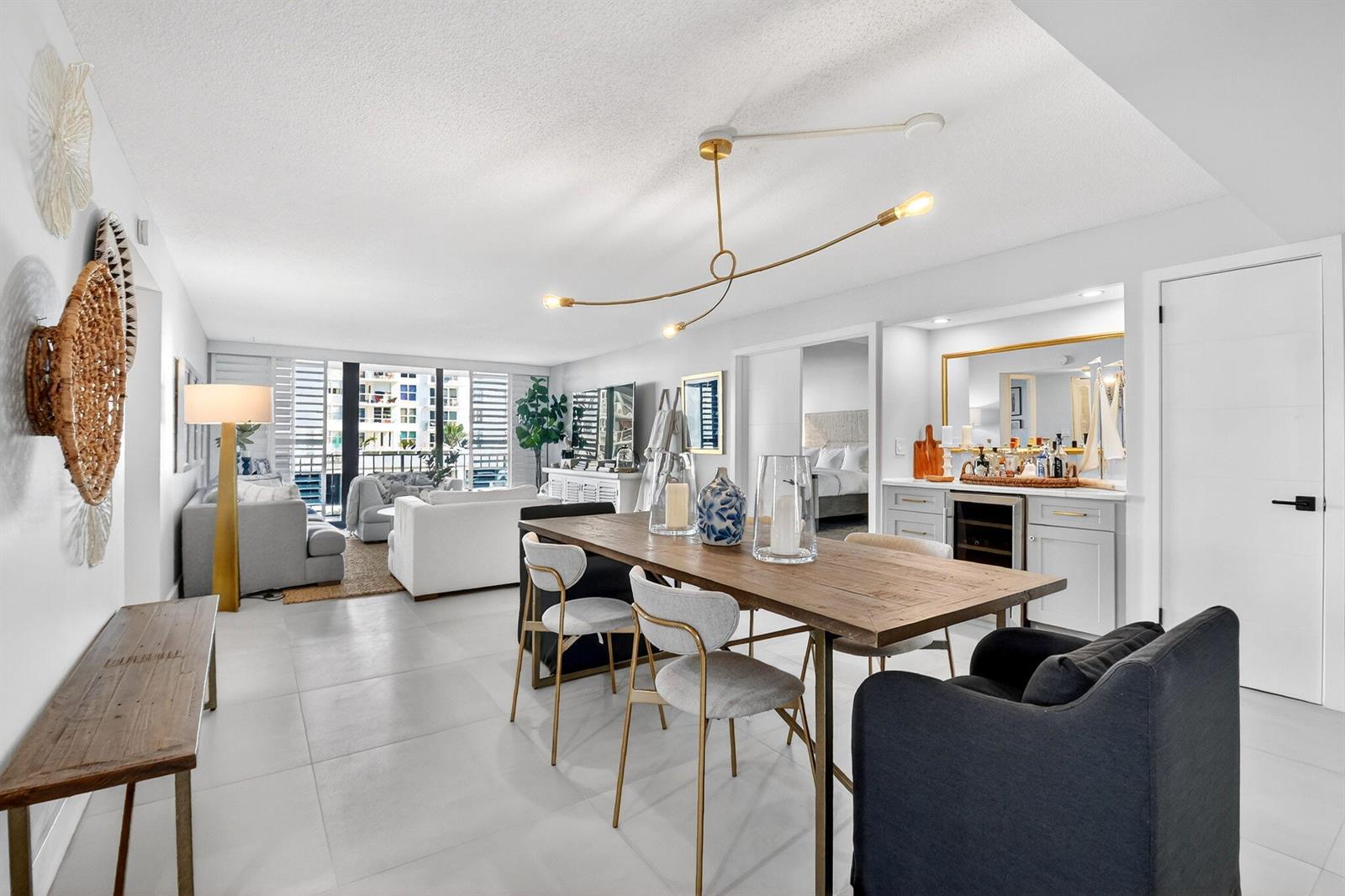 A bright, open-concept dining and living area features a wooden table, modern lighting, and balcony — 3456 S Ocean Boulevard # 105, Palm Beach FL 33480, PALM BEACH, FL