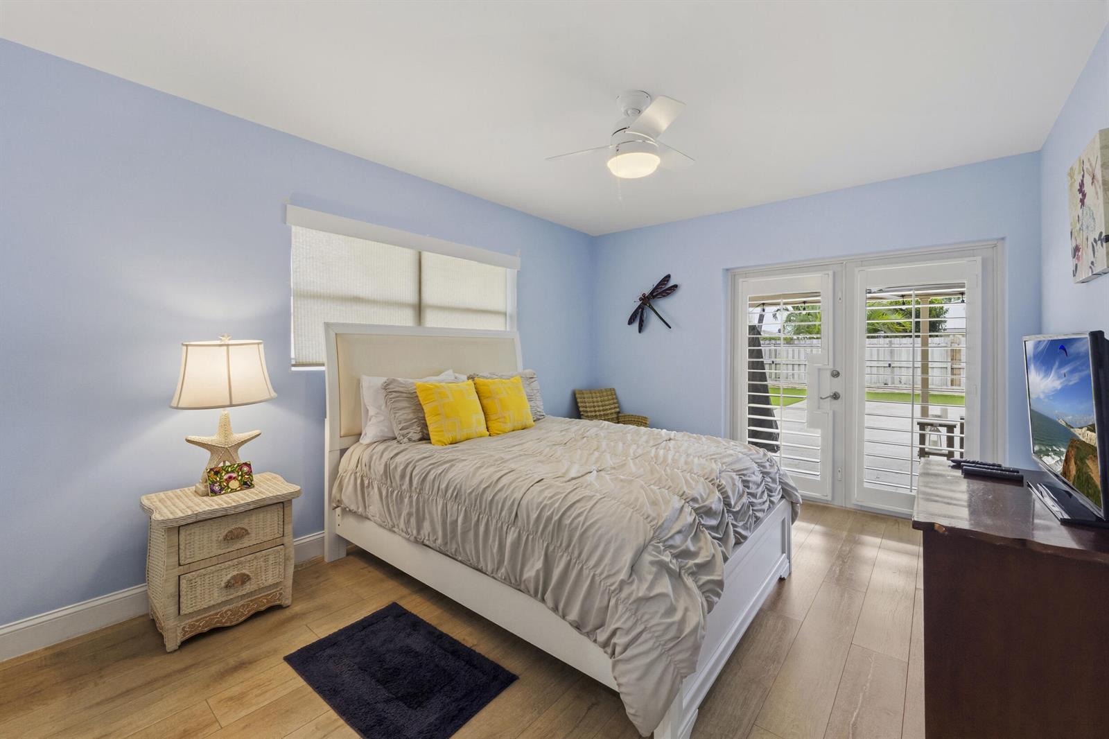 A bedroom with light blue walls, a white bed, a nightstand, and glass patio doors — 1205 Dolphin Road, Singer Island FL 33404, SINGER ISLAND, FL