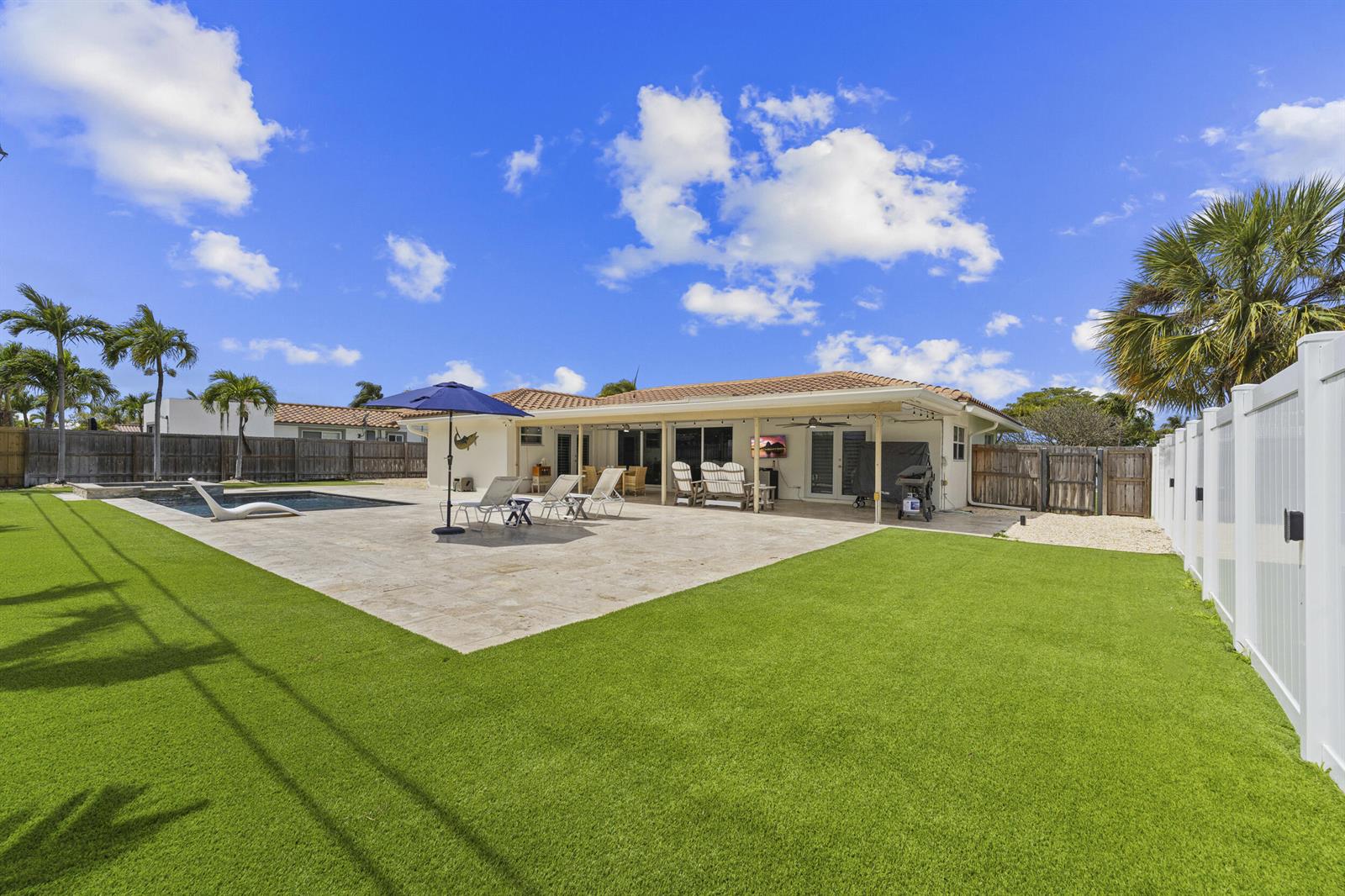 A backyard features a swimming pool, a stone patio, and a covered porch with furniture — 1205 Dolphin Road, Singer Island FL 33404, SINGER ISLAND, FL