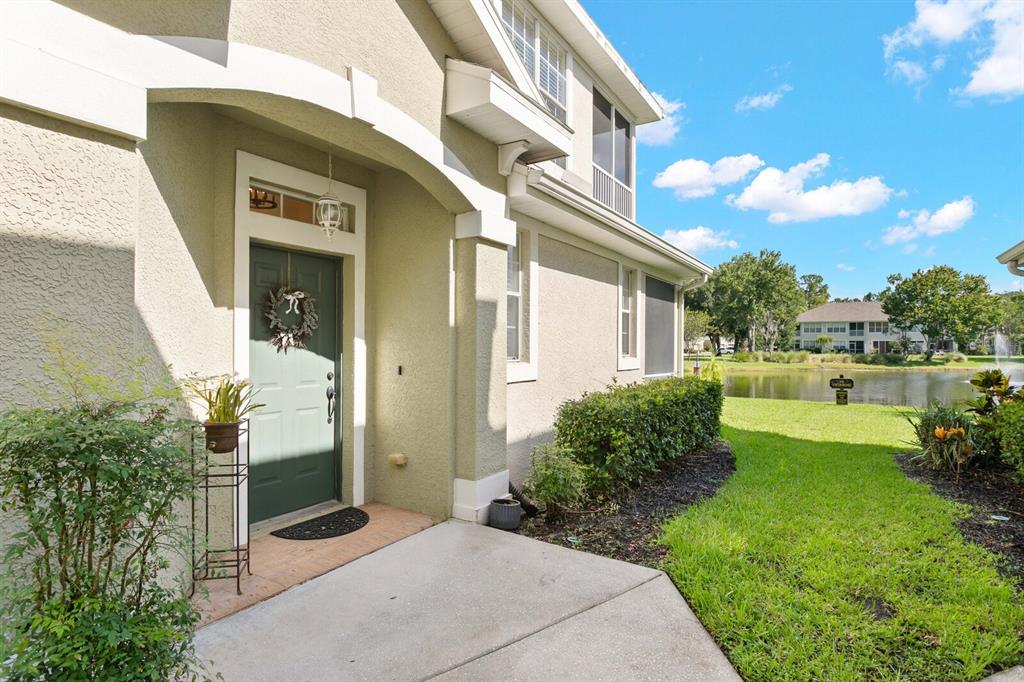 A green front door with a wreath sits under a covered entryway beside a pond — 14034 WATERVILLE CIRCLE, TAMPA, FL