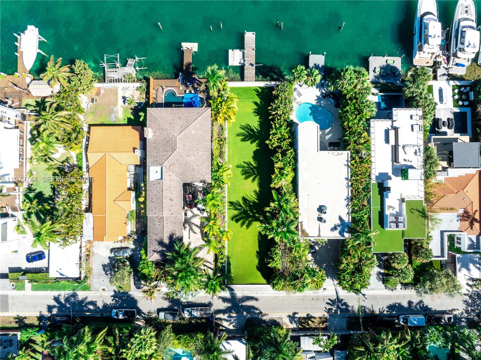 An aerial view shows waterfront residential properties with swimming pools, docks, and lush landscaping — 253 N Coconut Ln, Miami Beach FL 33139, MIAMI BEACH, FL