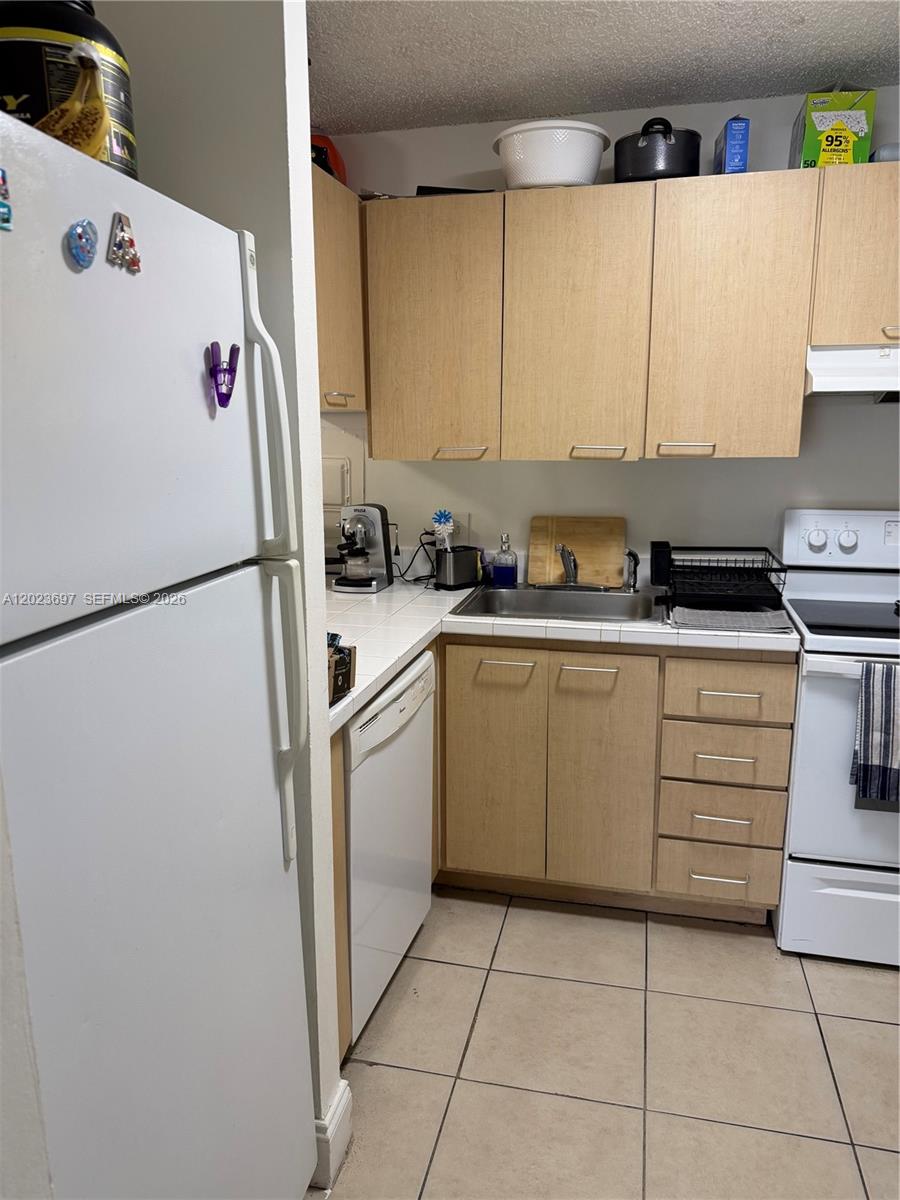 A kitchen features light wood cabinets, white appliances, a tiled countertop, and a tiled floor — 13789 SW 66th St # 283F, Miami FL 33183, MIAMI, FL
