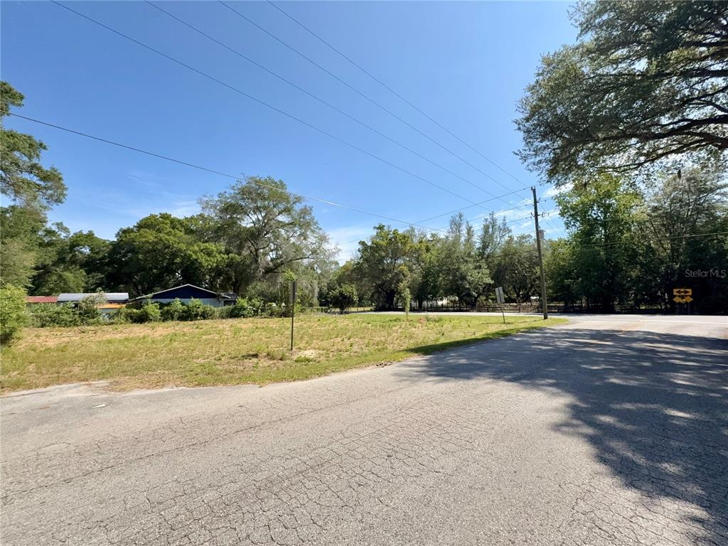 A vacant, grassy lot sits at a street corner near trees and power lines — TBD NW 12TH LANE, MORRISTON, FL
