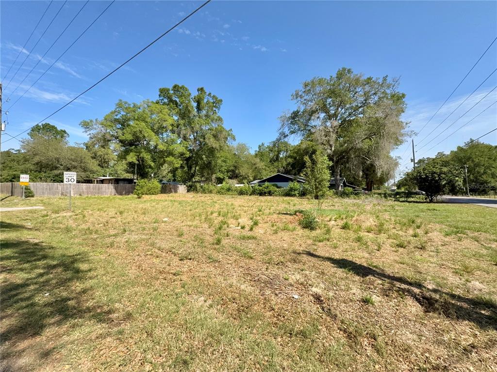 A vacant, grassy lot with scattered trees and a wooden fence under a blue sky — TBD NW 12TH LANE, MORRISTON, FL