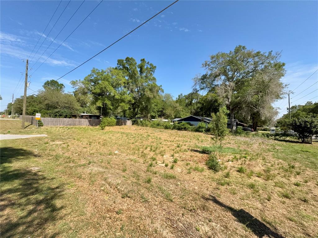 A vacant, grassy lot with trees and neighboring houses under a clear blue sky — TBD NW 12TH LANE, MORRISTON, FL