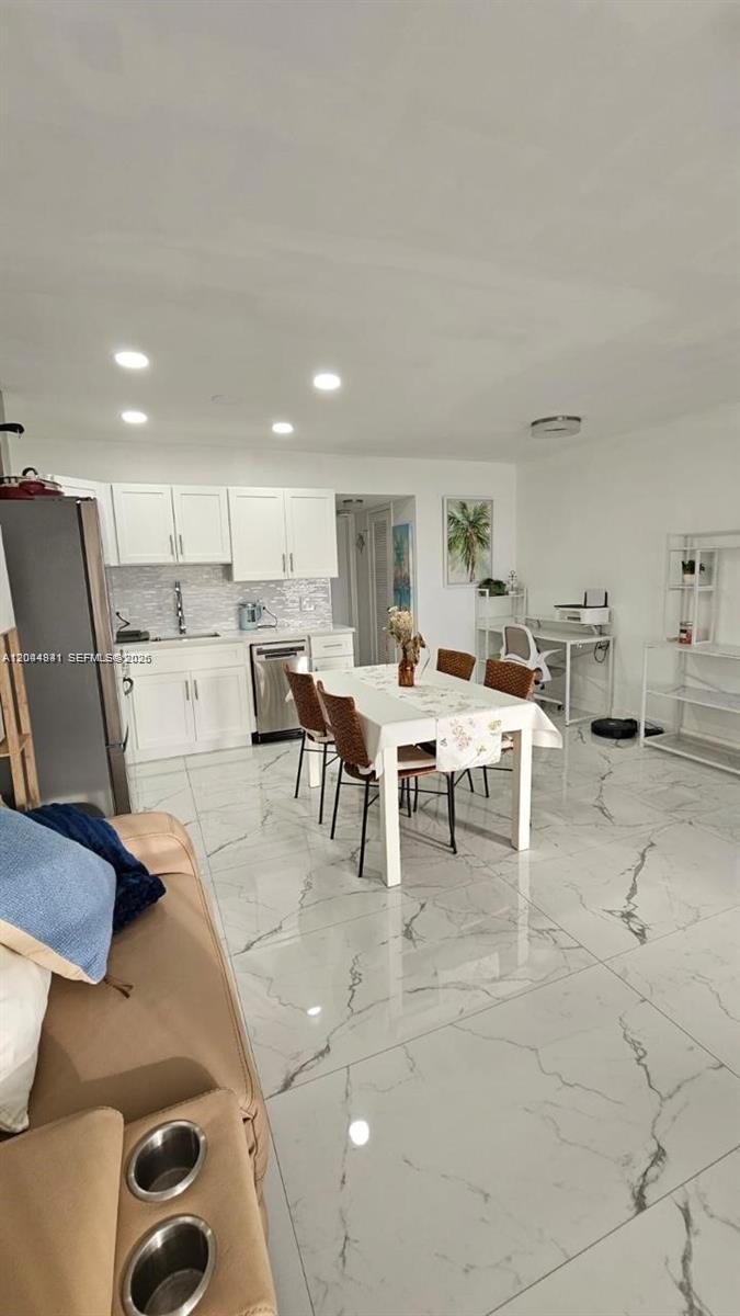 This open-concept kitchen and dining area features white cabinetry, marble-look tile flooring, and a table — 340 S Oakridge  S # 340, Deerfield Beach FL 33442, DEERFIELD BEACH, FL