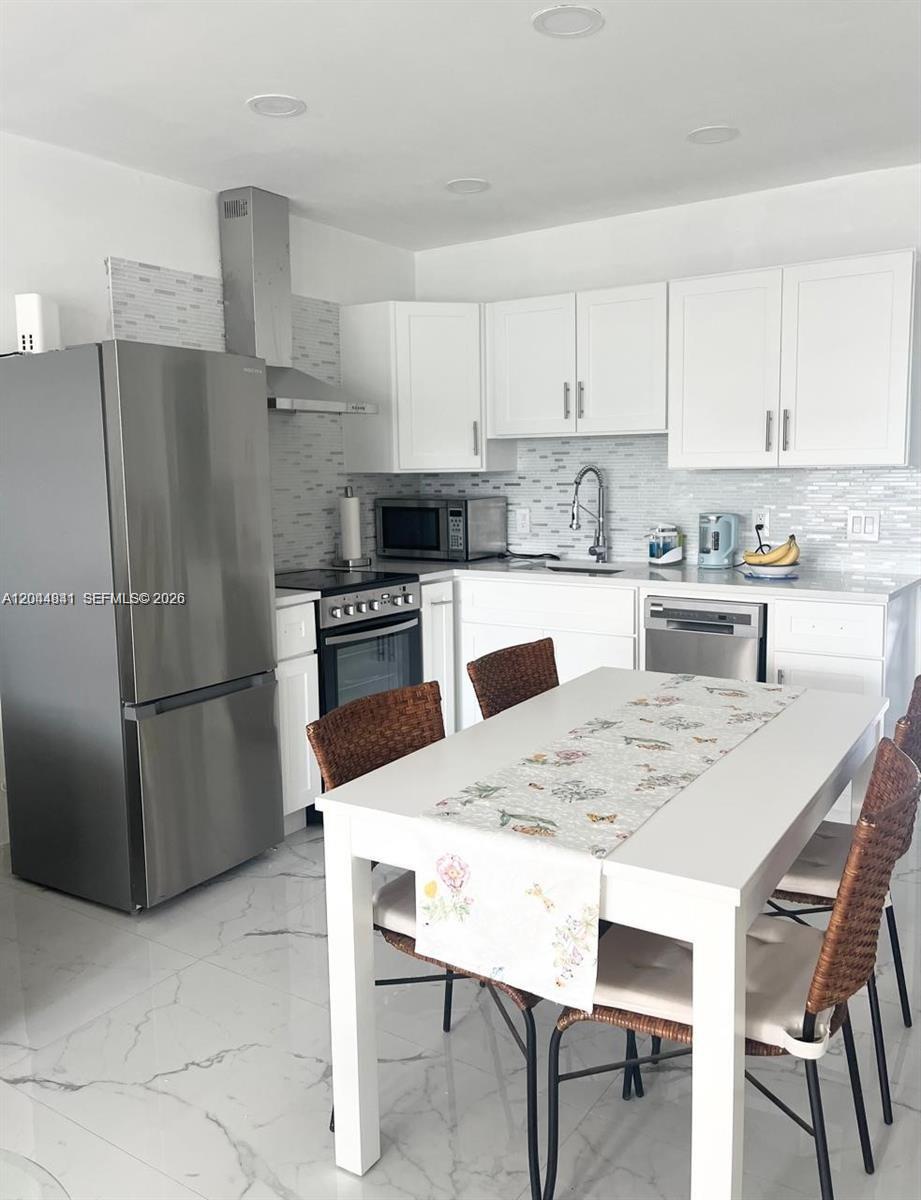 A modern kitchen features white cabinetry, stainless steel appliances, and a dining table with chairs — 340 S Oakridge  S # 340, Deerfield Beach FL 33442, DEERFIELD BEACH, FL