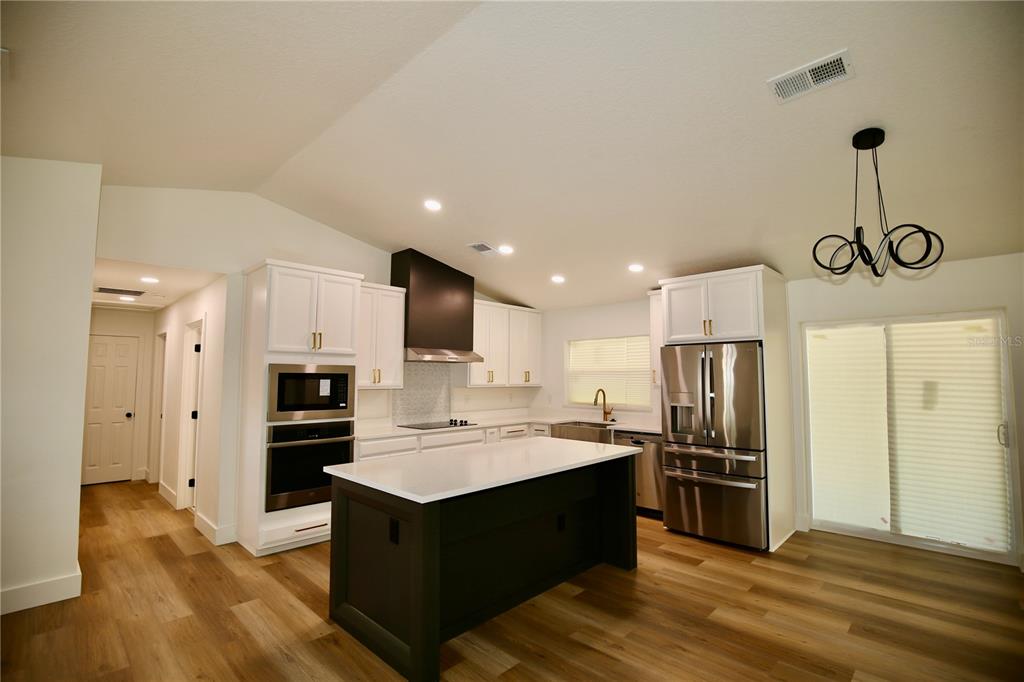 A modern kitchen features white cabinetry, a dark island, stainless steel appliances, and wood flooring — 2235 WAUTOMA PLACE, ORLANDO, FL