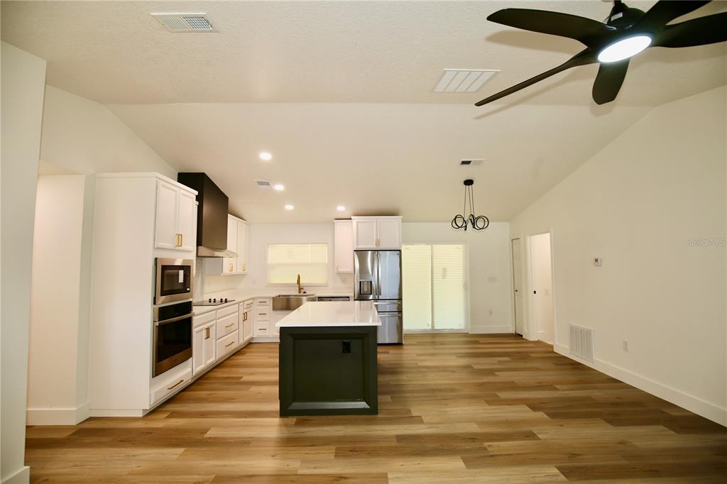 A modern kitchen features white cabinets, a dark island, stainless appliances, and wood-look flooring — 2235 WAUTOMA PLACE, ORLANDO, FL