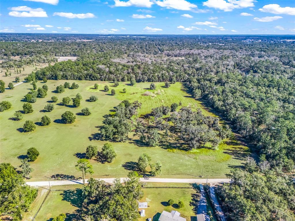 An aerial view shows a large, grassy field with scattered trees and a dirt road — TBD NW 127 COURT, OCALA, FL