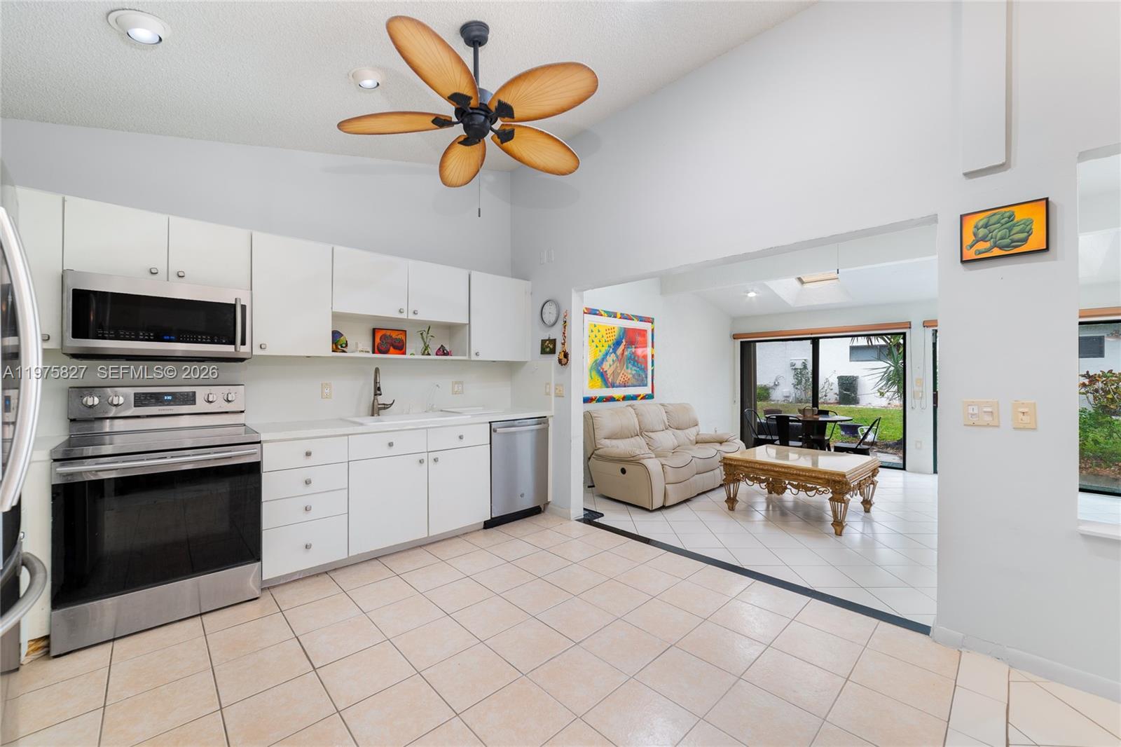 A kitchen with white cabinets and stainless steel appliances opens into a tiled living area — 3010 NW 12th St # D, Delray Beach FL 33445, DELRAY BEACH, FL
