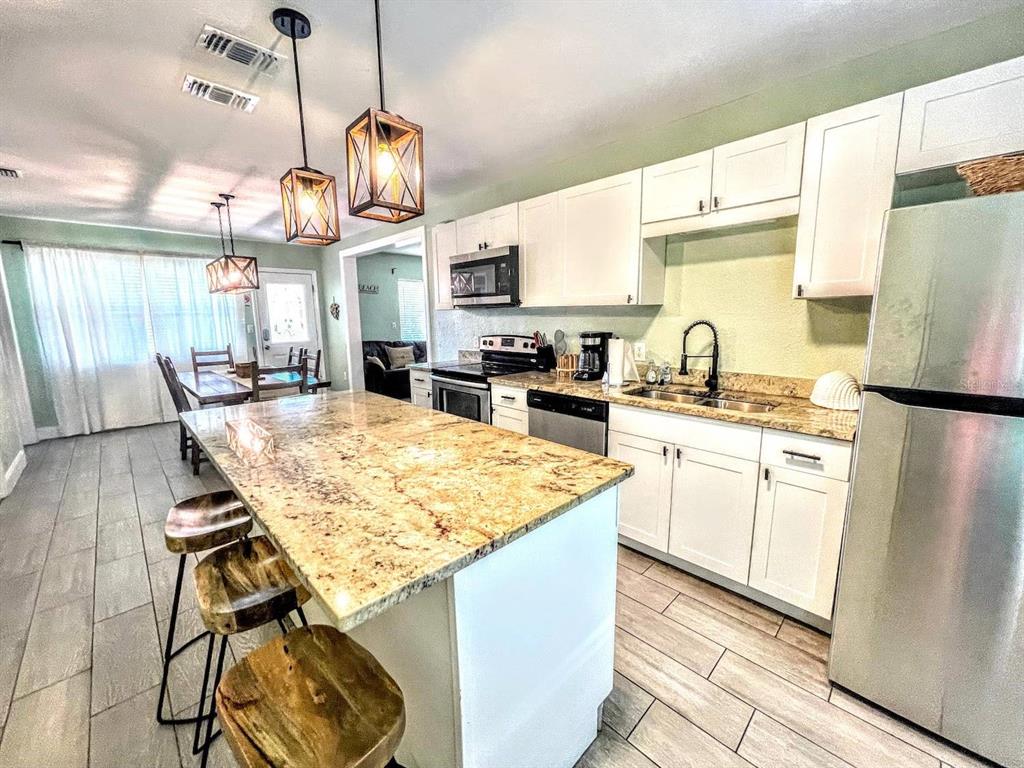 A kitchen features a granite-topped island, white cabinetry, stainless steel appliances, and wood-look tile flooring — 42 SOMERSET STREET, CLEARWATER BEACH, FL