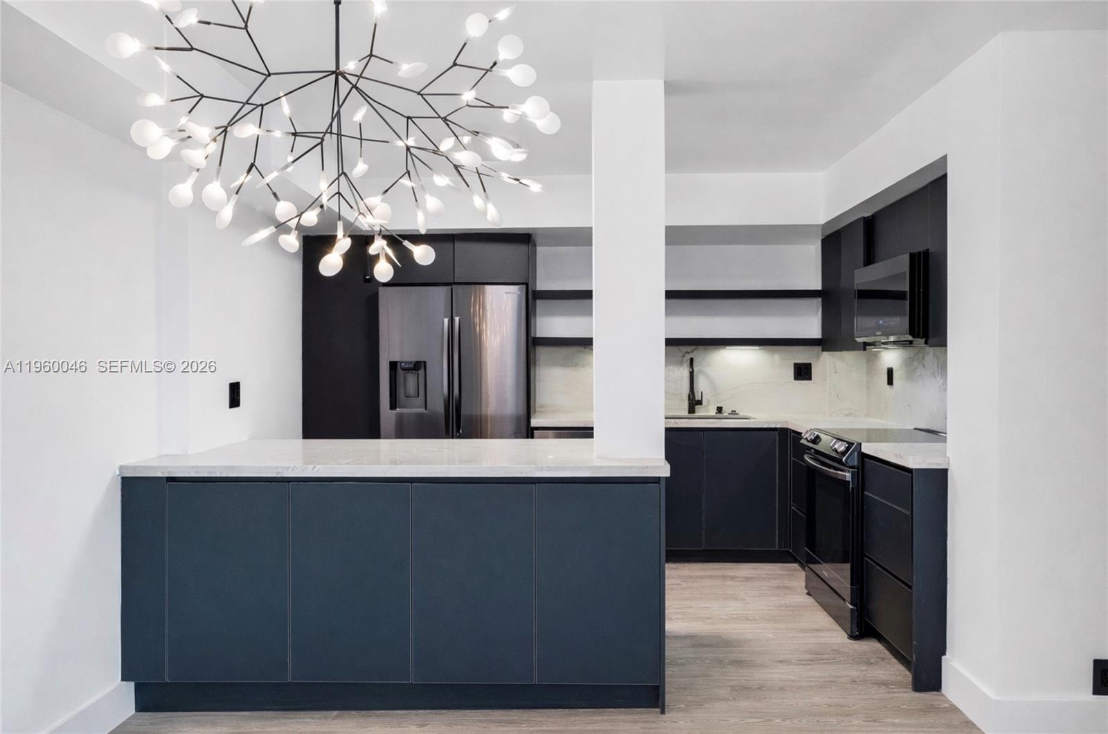 A modern kitchen features dark cabinetry, a marble-topped island, and a distinctive branching chandelier — 4000 Towerside Ter # 1509, Miami FL 33138, MIAMI, FL