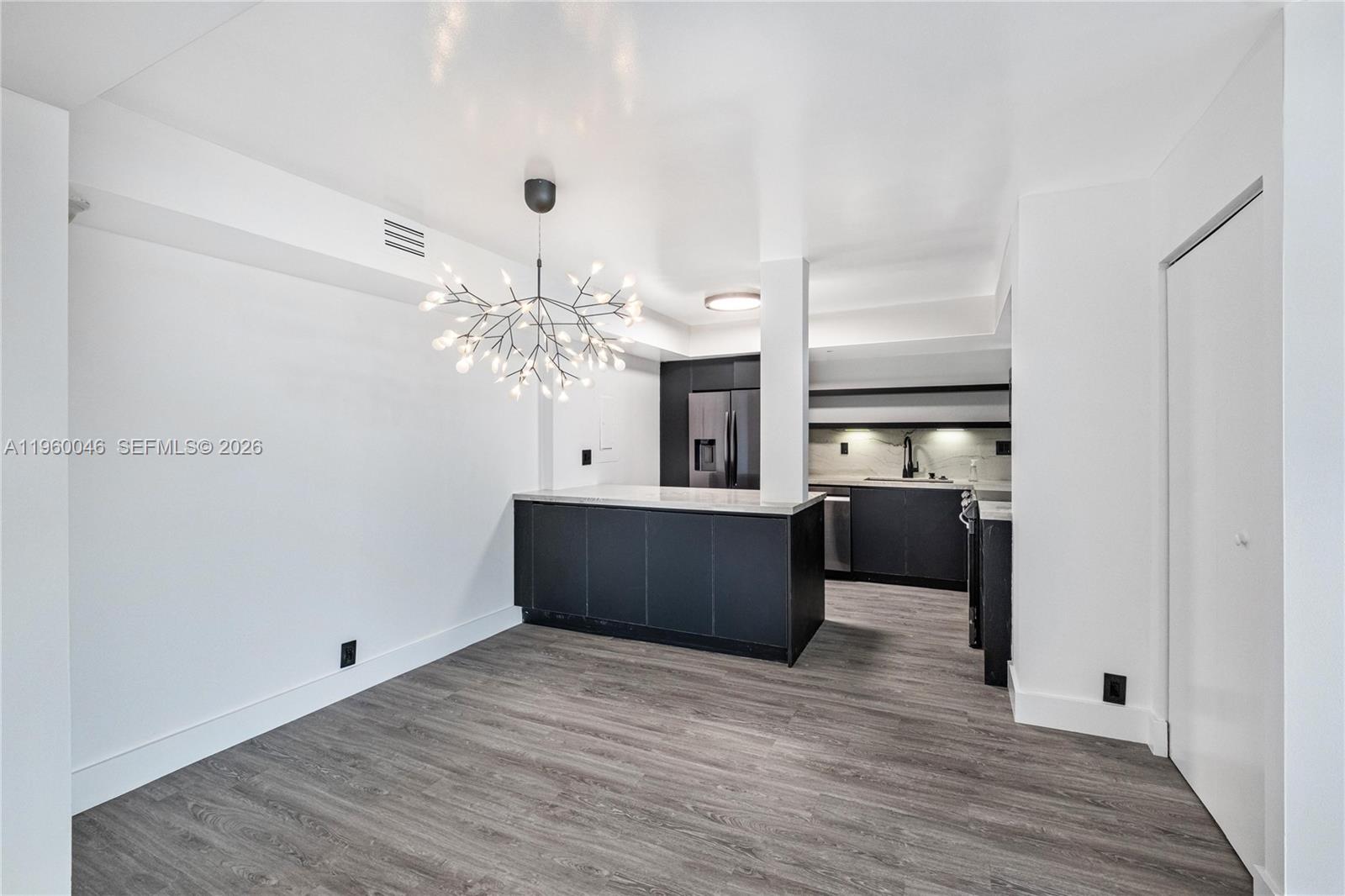 A modern kitchen features dark cabinetry, a central island, and a decorative branch-style chandelier — 4000 Towerside Ter # 1509, Miami FL 33138, MIAMI, FL