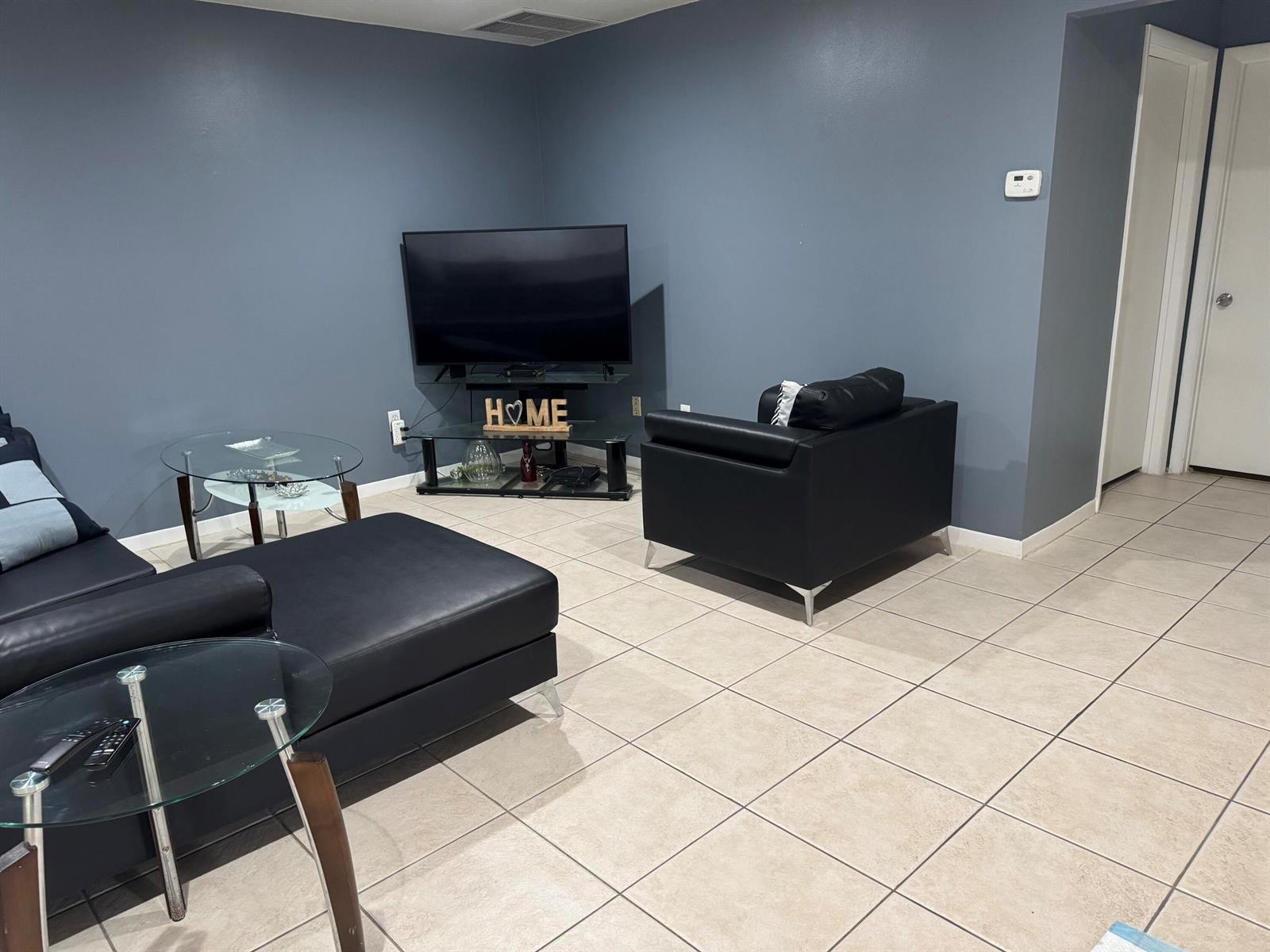A living room features blue walls, tile flooring, a black sectional, and a glass TV stand — 8016 AMBACH Way # 18D, Hypoluxo FL 33462, HYPOLUXO, FL