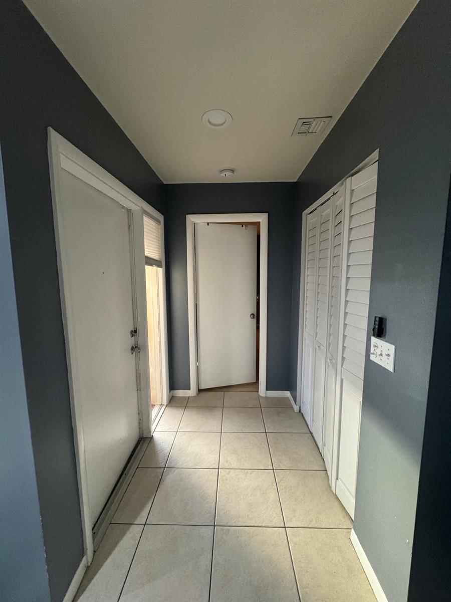 A hallway with dark blue walls, tile flooring, a white door, and louvered closet doors — 8016 AMBACH Way # 18D, Hypoluxo FL 33462, HYPOLUXO, FL