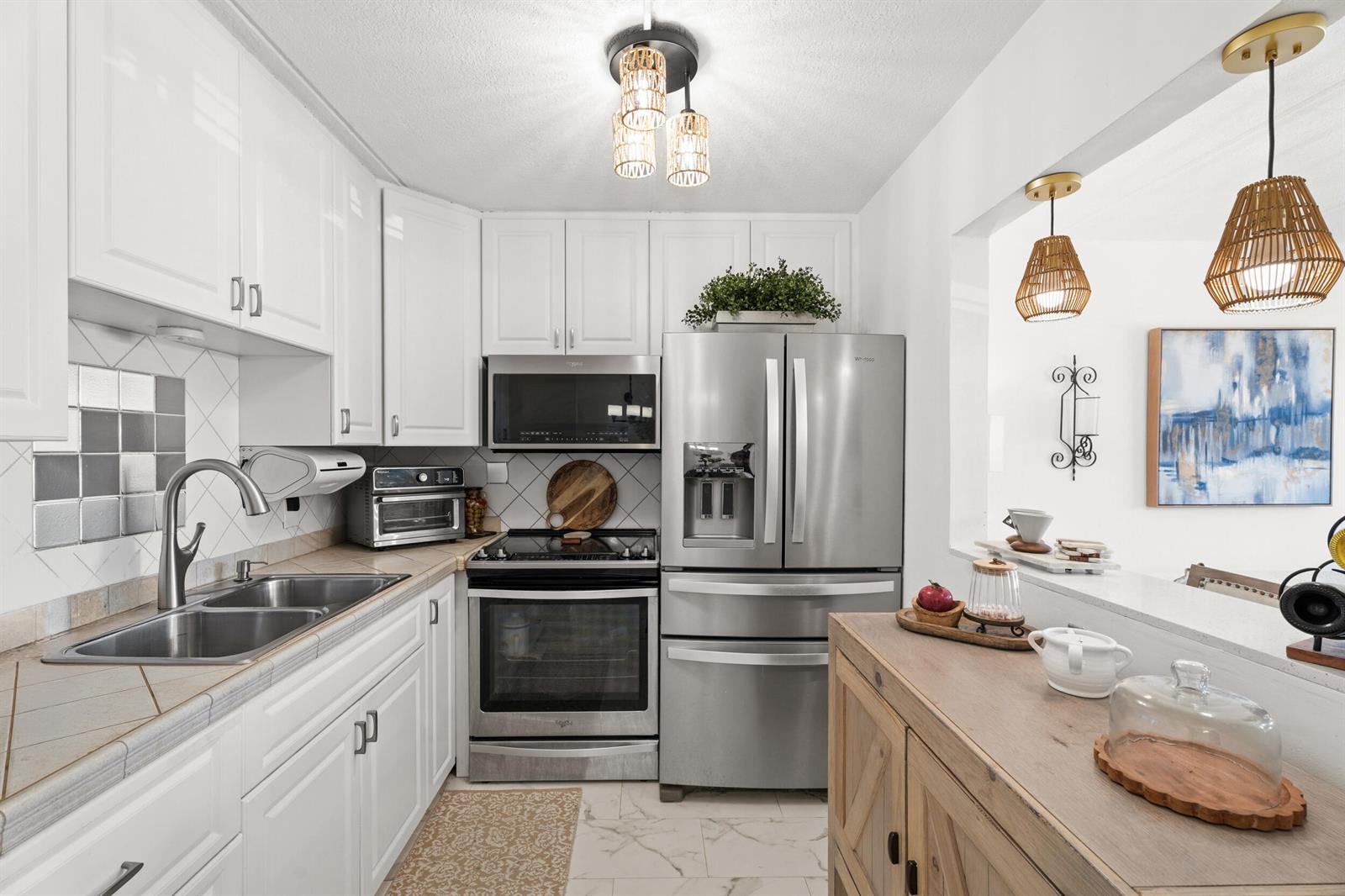 A kitchen features white cabinets, stainless steel appliances, tile countertops, and a wooden island — 200 Village Green Circle E # 206, Palm Springs FL 33461, PALM SPRINGS, FL