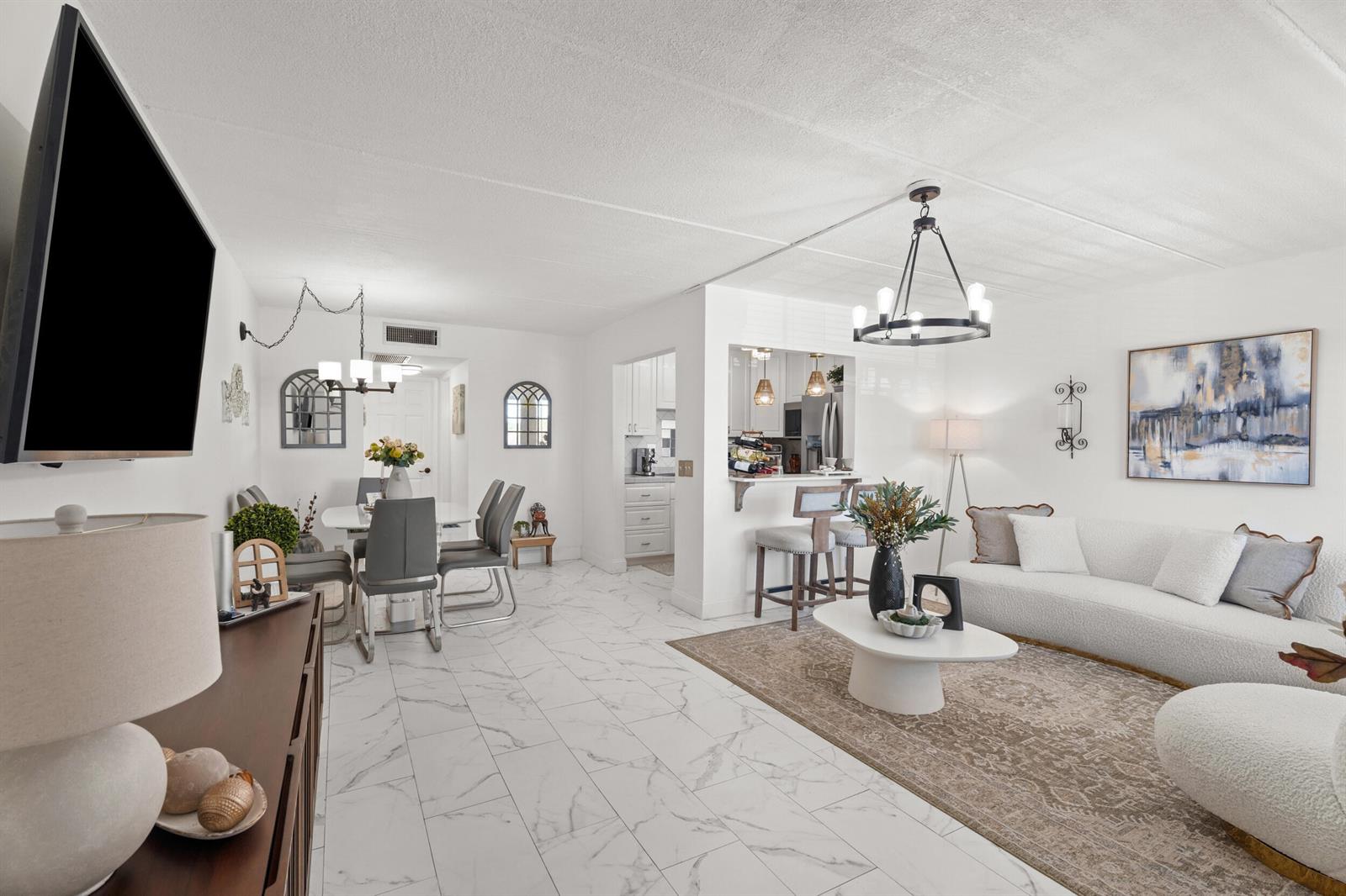 A bright, open-concept living and dining area features white marble-look tile flooring and modern decor — 200 Village Green Circle E # 206, Palm Springs FL 33461, PALM SPRINGS, FL