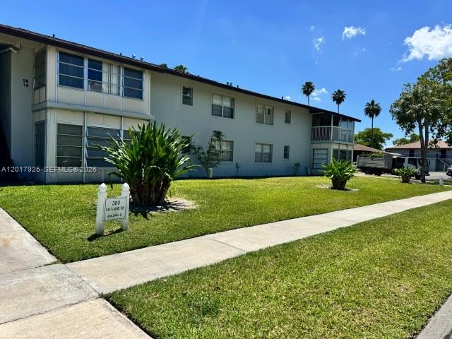 A two-story apartment building features light-colored siding, screened balconies, and a manicured lawn — 380 E Laurel Dr # 4D, Margate FL 33063, MARGATE, FL