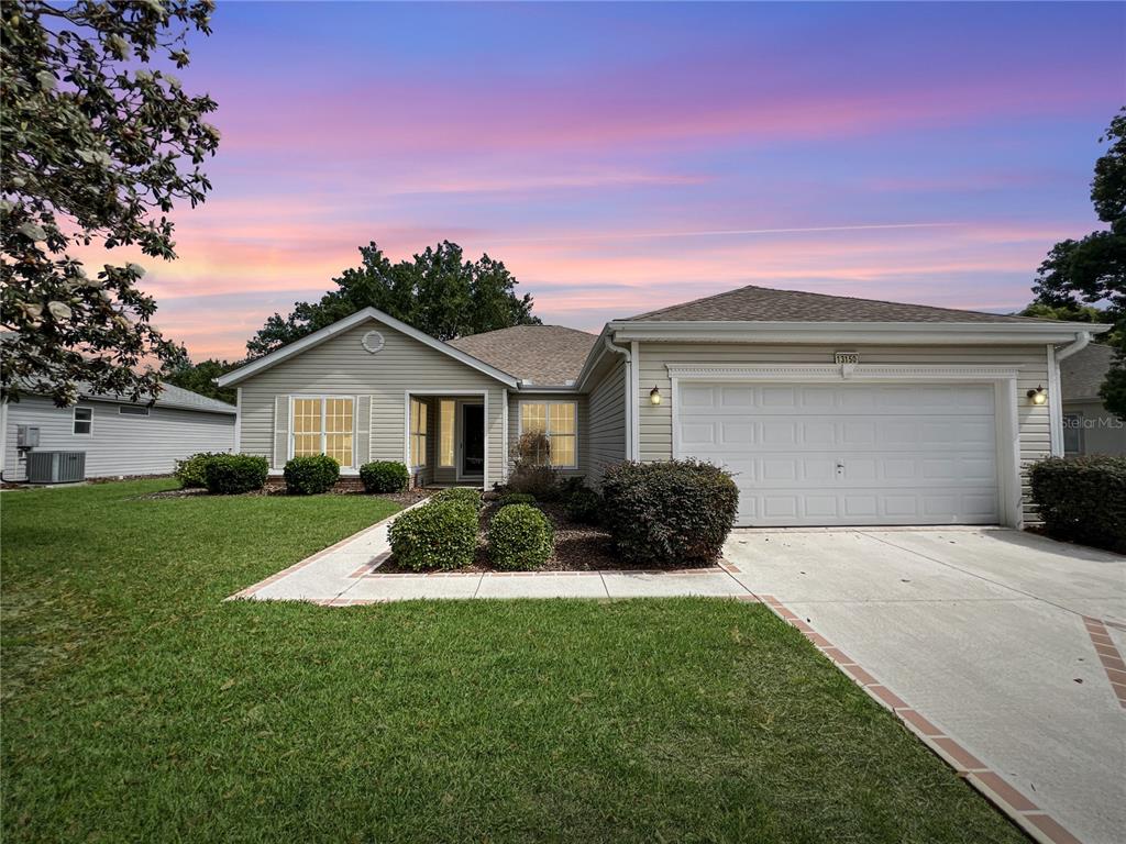 A single-story house with light siding, a two-car garage, and a landscaped front yard — 13150 SE 93RD CIRCLE, SUMMERFIELD, FL