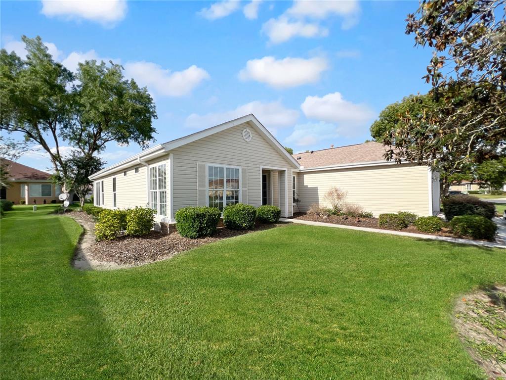 A light-colored, single-story suburban house with vinyl siding and a manicured lawn — 13150 SE 93RD CIRCLE, SUMMERFIELD, FL